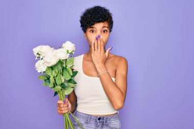 Güzel Afro-Amerikan kadın elinde bir buket beyaz çiçekle mor arkaplanı örtüyor. Ağzı, utancından ağzı açık kalmış, korku ifadesi, sessizlikten korkan, gizli bir konsept.