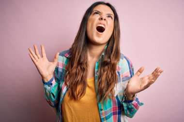 Genç, güzel, esmer, sıradan bir gömlek giyen, pembe arka planda duran çılgın, deli gibi bağıran, agresif bir ifade ve kollarla bağıran bir kadın. Hayal kırıklığı konsepti.