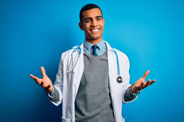 ハンサムなアフリカ系アメリカ人医師男身に着けているコートと聴診器上の青の背景笑顔陽気にオープン腕として優しい歓迎 正と自信を持って挨拶 — ストック写真