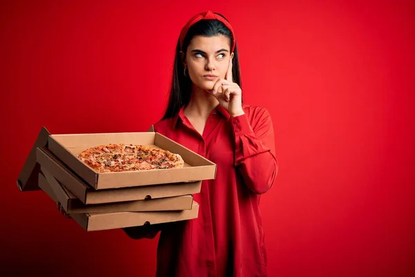 若いです美しいですブルネット女性保持配達ボックスとともにイタリアのピザ以上赤の背景深刻な顔考える上で質問 非常に混乱したアイデア — ストック写真