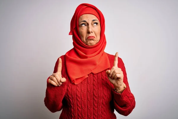 中世のブルネット女性身に着けていますムスリム伝統的なヒジャーブ上の隔離された白い背景上に上を向いて悲しいと動揺 指で方向を示す 不幸なと落ち込んで — ストック写真