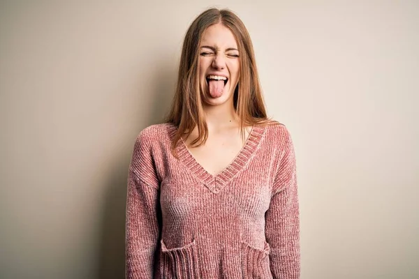 年轻美丽的红头发女人穿着粉色休闲衫 披着孤立的白色背景 带着滑稽的表情伸出舌头 情感概念 — 图库照片
