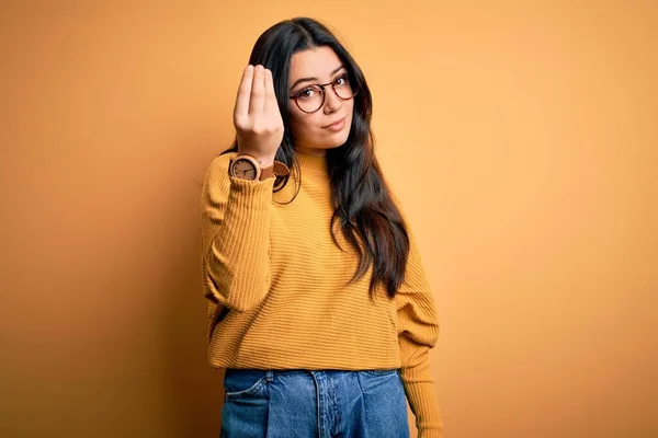 若いですブルネット女性身に着けている眼鏡とカジュアルなセーター上の黄色隔離された背景イタリアのジェスチャーとともに手と指の自信のある式 — ストック写真