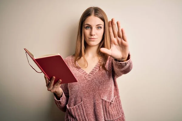 年轻美丽的红头发女学生在孤零零的白色背景上读着书 张开手 做手势 严肃而自信地表达着自己的防卫姿态 — 图库照片
