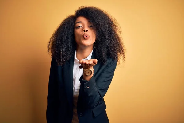 Young beautiful african american business woman with afro hair wearing elegant jacket looking at the camera blowing a kiss with hand on air being lovely and sexy. Love expression.