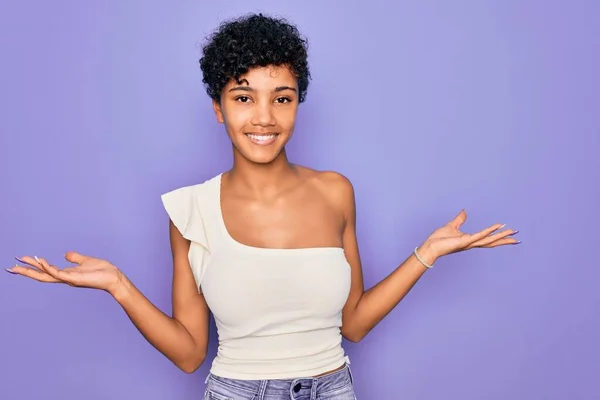 年轻美丽的非洲裔美国女人 身穿浅紫色背景的休闲T恤 微笑着张开双手 展示和宣传比较与平衡 — 图库照片