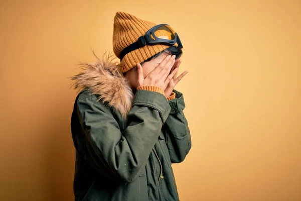 泣きながら手で顔を覆う悲しい表情で黄色の背景にスキーゴーグルを使用して雪のスポーツウェアを身に着けている美しいアジアのスキー少女 うつ病の概念 — ストック写真