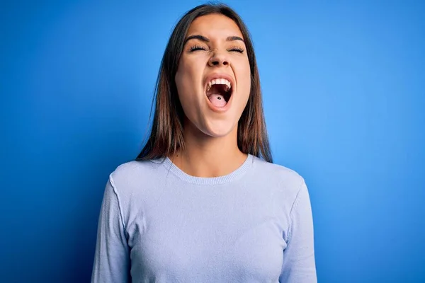 若い美しいブルネットの女性は怒りで叫んで 怒りで叫んで 青の背景怒りと怒りの上に立ってカジュアルなセーターを着ています 激怒と積極的な概念 — ストック写真