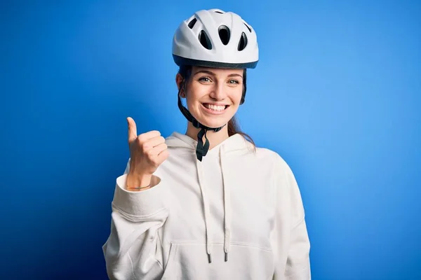 孤立した青の背景の上に自転車のヘルメットを身に着けている若い美しい赤毛のサイクリストの女性は 手で幸せな親指アップジェスチャーを行います 成功を示すカメラを見て表現を承認する — ストック写真