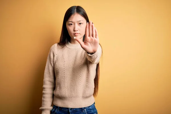 年轻美丽的亚洲女人穿着休闲装 披着黄色孤立的背景 手心紧握 停止歌唱 脸上带有消极而严肃的手势的警告表情 — 图库照片