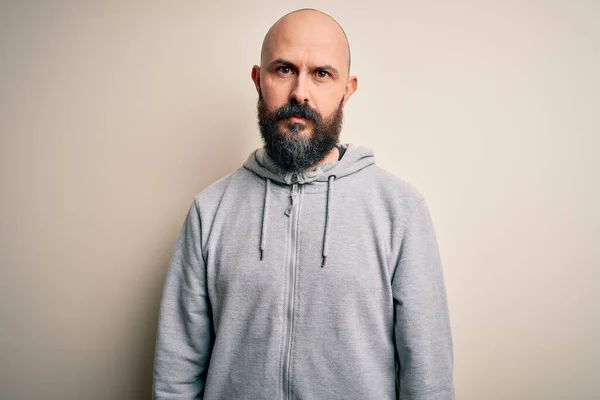 Handsome sporty bald man with beard wearing sweatshirt standing over pink background with serious expression on face. Simple and natural looking at the camera.