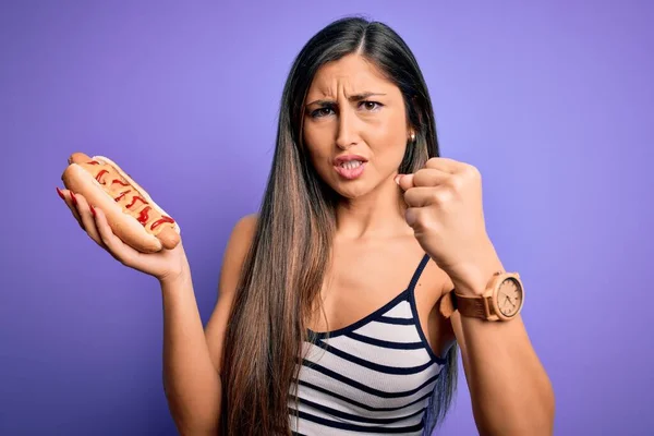 Jonge Vrouw Eten Hotdog Met Ketchup Mosterd Paarse Achtergrond Geïrriteerd — Stockfoto