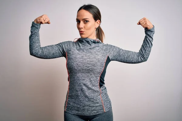 Young blonde fitness woman wearing sport workout clothes over isolated background showing arms muscles smiling proud. Fitness concept.