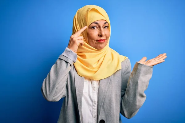 青の背景にイスラム教徒の伝統的なヒジャーブを身に着けている中世のブルネットのビジネス女性は混乱し コピースペースを示し 額に指を指すオープンヤシに悩まされました 考えてみて — ストック写真