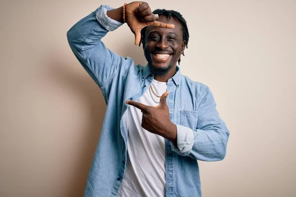 Young handsome african american man wearing casual denim shirt over white background smiling making frame with hands and fingers with happy face. Creativity and photography concept.