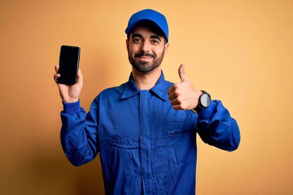 Μηχανικός Γενειάδα Φορώντας Μπλε Στολή Και Καπάκι Κρατώντας Smartphone Που — Φωτογραφία Αρχείου