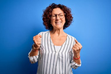 Orta yaşlı, güzel kıvırcık saçlı, sıradan çizgili tişört giyen, başarılı olmak için heyecanlı kollarını kaldırmış ve gözleri kapalı zaferi kutlayan bir kadın. Kazanan konsept.