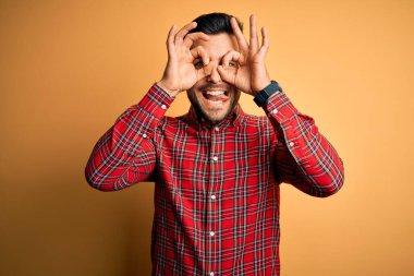 Sarı arka plan üzerinde duran sıradan tişörtlü genç yakışıklı bir adam. Dürbün gibi güzel hareketler yapıyor, gözleri parmaklarından bakıyor. Çılgın ifade.