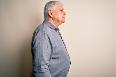 Kıdemli yakışıklı beyaz gömlekli adam, izole edilmiş beyaz arka planda duruyor, yan yana bakıyor, rahat profil pozu veriyor, kendine güvenen bir gülümsemeyle doğal bir poz veriyor..