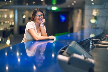 Mutlu ve kendinden emin gülümseyen genç ve güzel bir kadın. Yüzünde gülümsemeyle restorandaki tezgah demirine yaslanarak oturmak.