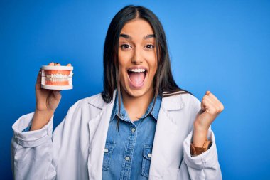 Plastik diş protezi taşıyan güzel, esmer dişçi kadın gururla bağırıyor ve zaferi ve başarıyı kutluyor.