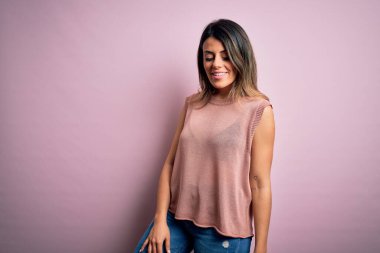 Moda kıyafetleri giyen genç ve güzel bir kadın. Manken, sokak tarzı giyiniyor. Pembe arka planda dikiliyor.