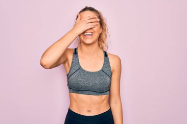 Mavi gözlü genç, sarışın spor kadın spor kıyafetleri giyerek spor yapıyor. Gülümsüyor ve yüz yüze gülüyor. Şaşırtmak için gözleri örtüyor. Kör kavram.