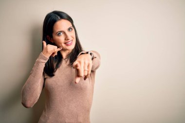 Mavi gözlü genç esmer kadın izole edilmiş beyaz arka planda günlük süveter giyiyor gülümsüyor telefonda konuşuyor ve seni işaret ediyor. Ara beni..