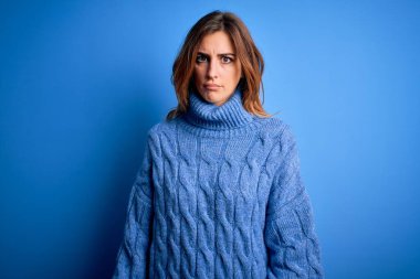 Genç, güzel, esmer bir kadın mavi arka plan kuşkucu ve gergin üzerine balıkçı yaka kazak giyiyor. Problemden dolayı üzgün. Negatif kişi.