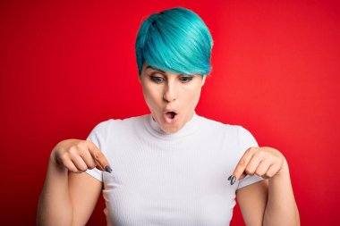 Mavi saçlı, kırmızı arka planda sıradan tişörtler giyen genç ve güzel bir kadın. İlan veren parmaklarıyla işaret ediyor. Şaşırmış bir yüz ve açık bir ağız.