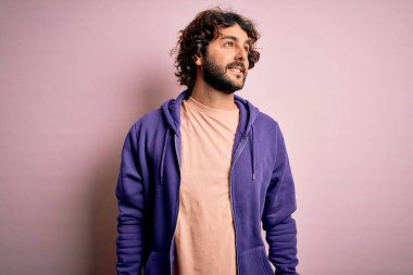 Sakallı, pembe arka planda sıradan bir kazak giyen, yüzünde gülümseme ve doğal bir ifadeyle yan yana bakan genç, yakışıklı bir sporcu. Kendinden emin gülen.