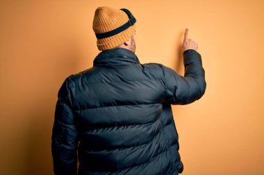 Kar giysileri ve kayak gözlüğü takan sakallı yakışıklı kayakçı geriye doğru poz veriyor.