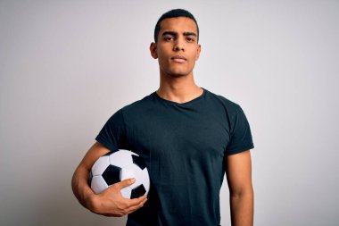 Beyaz arka planda futbol topu tutan yakışıklı Afro-Amerikalı adam yüzünde ciddi bir ifadeyle rahatladı. Basit ve doğal bir şekilde kameraya bakıyorsun..