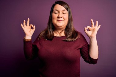 Güzel esmer ve cüsseli bir kadın izole edilmiş mor arka plan üzerine gündelik bir süveter giyer rahatlar ve parmaklarıyla meditasyon hareketi yaparken gözleri kapalı gülümserler. Yoga konsepti.