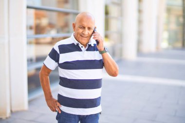 Kıdemli yakışıklı adam mutlu ve kendinden emin gülümsüyor. Yüzünde gülümsemeyle kasaba caddesinde telefonla konuşuyor.