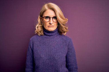 Orta yaşlı, güzel, mor balıkçı yaka kazak giyen, gözlüklü, bunalımlı, sıkıntılı, sinirli ve korkmuş bir sarışın kadın. Üzücü ifade.