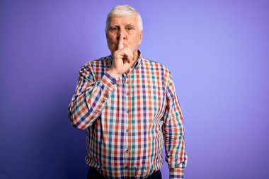 Üst düzey yakışıklı, parlak gömlekli, soyutlanmış mor arkaplanlı, dudakları parmaklı, sessiz olmak isteyen bir adam. Sessizlik ve gizli konsept.