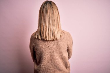 Pembe izole bir arka plan üzerine kışlık yün kazak giyen genç, güzel sarışın kadın geriye dönüp çapraz kollarla bakıyor.