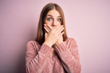 İzole edilmiş pembe arka plan üzerine gündelik kazak giyen genç, güzel, kızıl saçlı bir kadın yanlışlıkla ağzı ellerle kapatmış. Gizli konsept.