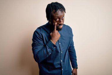 Genç, yakışıklı, Afro-Amerikalı bir adam beyaz arka planda dikilmiş, senin jestini seyrediyor. Şüpheli bir ifade.