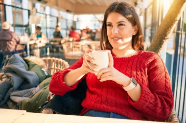 Genç ve güzel esmer kadın mutlu ve kendinden emin gülümsüyor. Yüzünde gülümsemeyle oturmuş restoranda bir fincan kahve içiyorum.