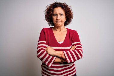 Orta yaşlı güzel kıvırcık saçlı kadın beyaz arka planda çizgili süveter giyiyor şüpheci ve gergin, yüzünde çapraz kollu tasvip etmeyen bir ifade var. Negatif kişi.