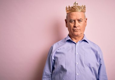 Middle age hoary man wearing golden crown of king standing over isolated pink background with serious expression on face. Simple and natural looking at the camera. clipart