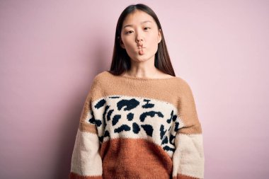 Genç ve güzel Asyalı kadın pembe izole edilmiş arka plan üzerine hayvan desenli süveter giyip dudaklarıyla balık suratı yapıyor, çılgınca ve komik bir jest. Komik ifade.