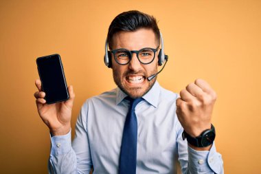 Çağrı merkezinden gelen müşteri hizmetleri kulaklığı takan bir işletmeci akıllı telefon ekranında sinirli ve sinirli bir şekilde bağırıyor, deli gibi bağırıyor ve elini kaldırarak bağırıyor.