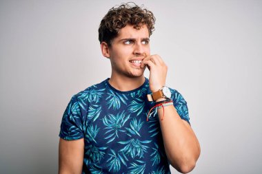 Sarışın, tatilde, kıvırcık saçlı, sıradan bir tişört giyen gergin ve gergin görünen dudakları tırnak yiyen genç bir adam. Endişe sorunu.