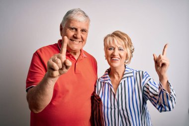 Üst düzey güzel çift soyutlanmış beyaz arka planda bir numaralı parmağı gösterip işaret ederken kendinden emin ve mutlu gülümsüyor..