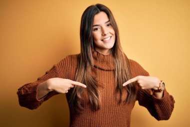 İzole edilmiş sarı arka planda dikilen sıradan bir süveter giyen genç ve güzel bir kız yüzünde bir gülümsemeyle gururla ve mutlu bir şekilde kendini işaret ediyor..