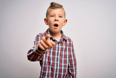 Mavi gözlü, zarif gömlekli küçük beyaz bir çocuk izole edilmiş arka planda dikiliyor. Kameraya kızgın ve sinirli olduğunu gösteriyor.