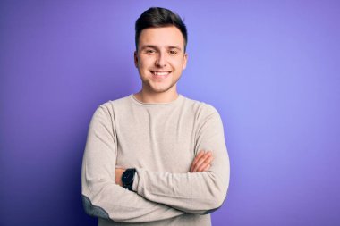 Mor izole edilmiş arka planda sıradan bir süveter giyen, kollarını kavuşturup kameraya gülümseyen yakışıklı beyaz bir adam. Pozitif kişi.